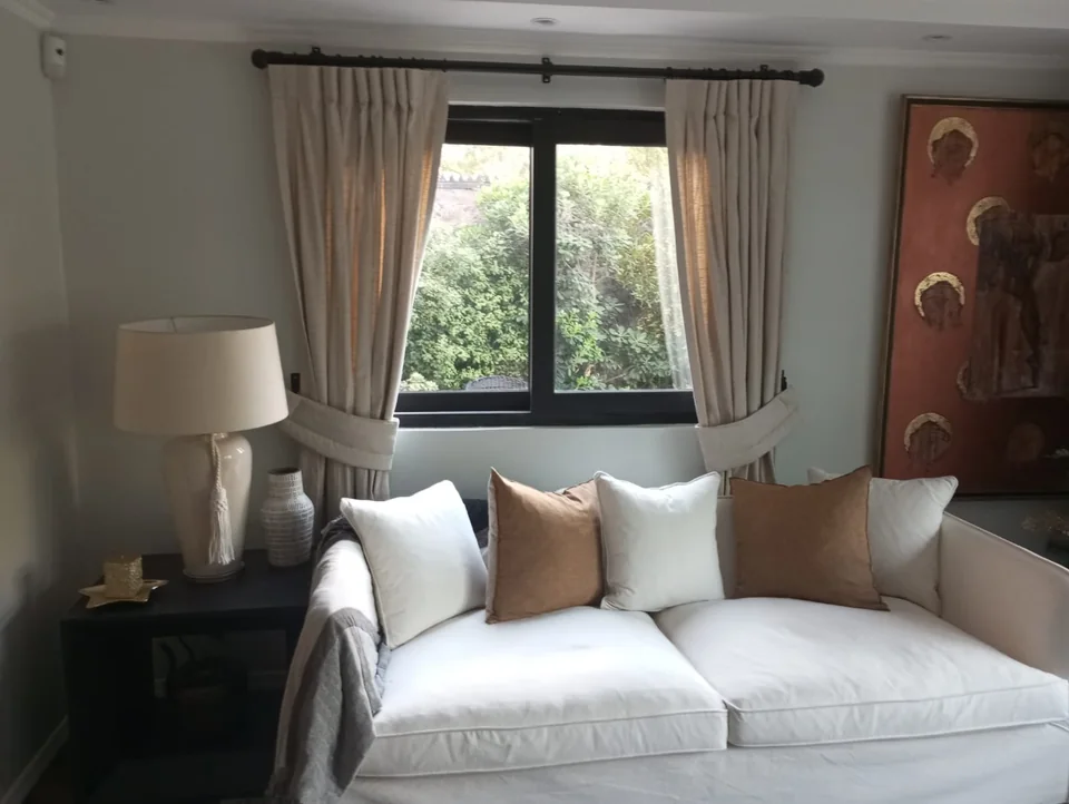 Cortinas de tela en tonos claros junto a un ventanal y un sofá